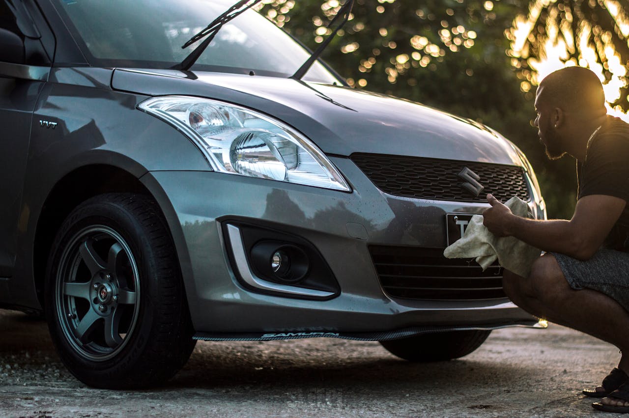 contact-img-01 A man carefully cleans a car hood at sunset, focusing on details.