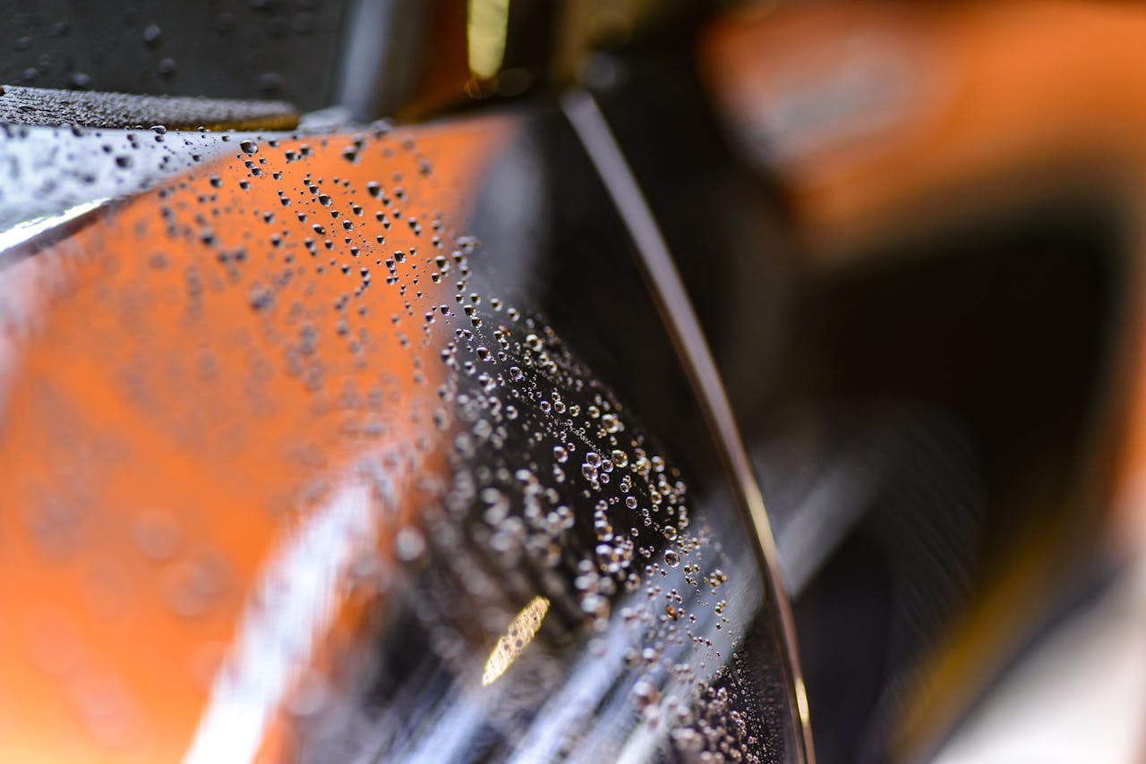 contact-img-02 Close-up view of water droplets on a glossy car surface with a blurred background.