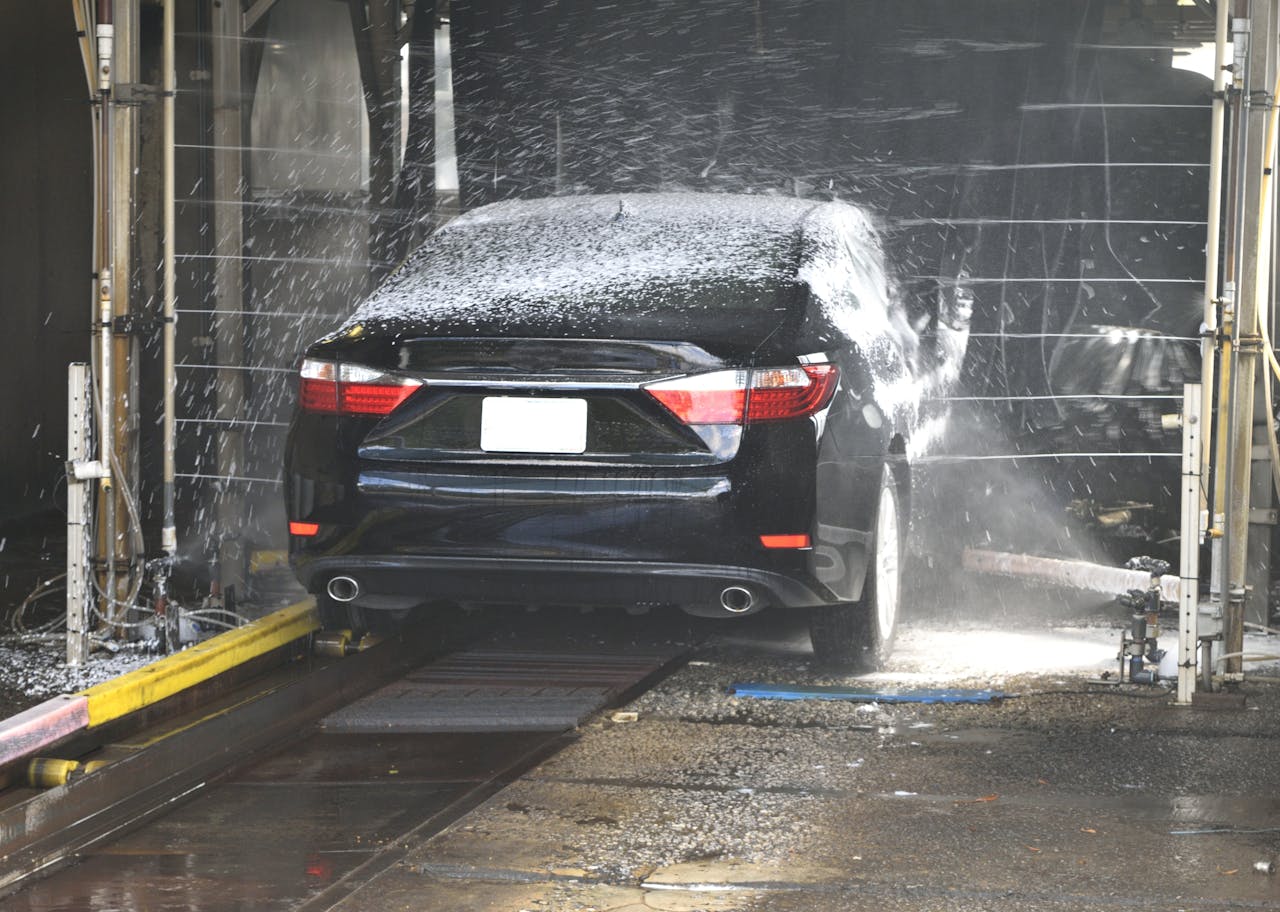 hero-img-01 A black car being cleaned in an automated car wash with water and foam.